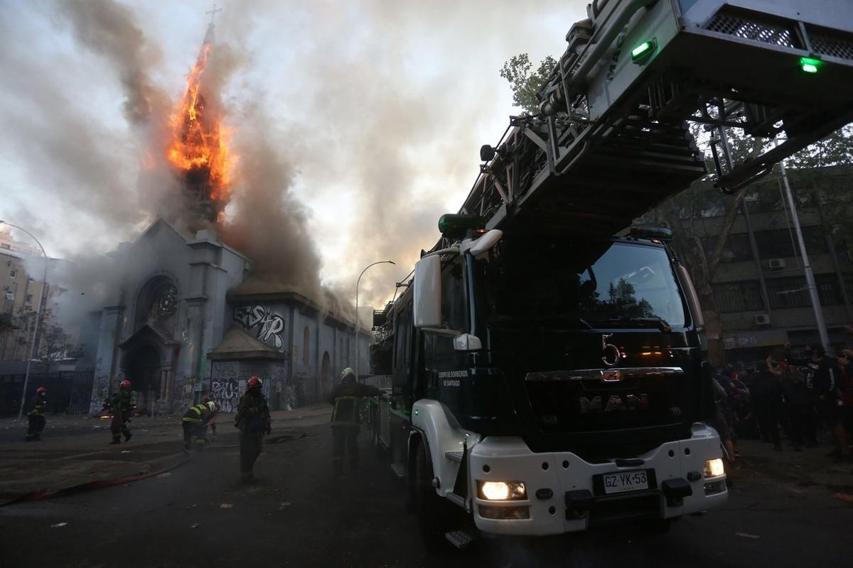 AME2281. SANTIAGO (CHILE), 18/10/2020.- Bomberos trabajan en la extinción del incendio de la Iglesia de La Asunción hoy domingo, en los alrededores de la Plaza Italia de Santiago (Chile), rebautizada popularmente como Plaza Dignidad, durante el primer aniversario de las protestas que sacudieron todo el país austral y que tuvieron su epicentro en la capital chilena. EFE/Elvis González