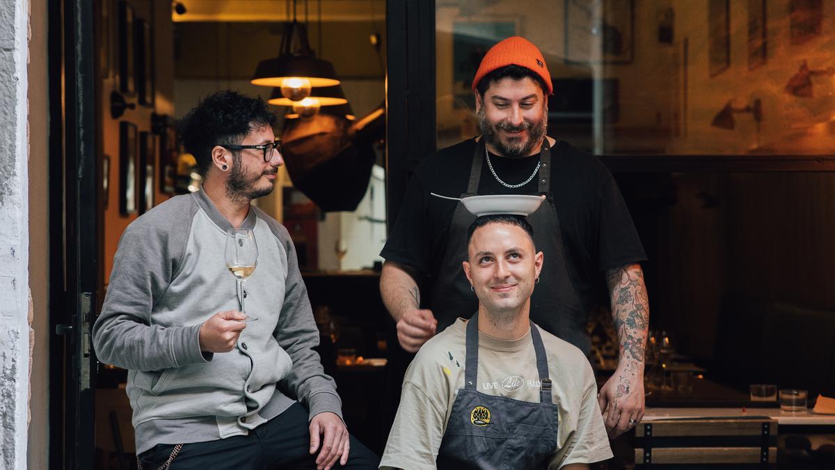 Diego y Marcos Amico observan cómo Simone Nizi sostiene un plato con la cabeza, en la puerta del restaurante Mama Gorda.