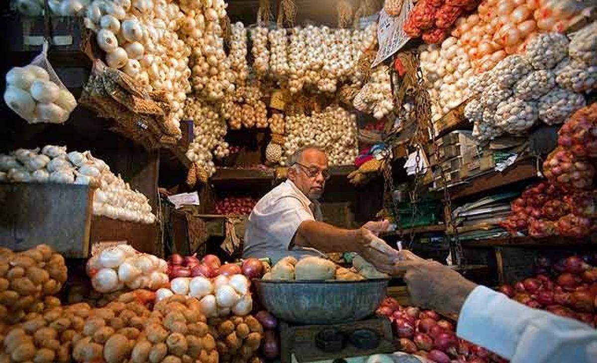 Un comerciant entrega el canvi a un client en una botiga de venda d’alls, cebes i patates al mercat de Mumbai (Índia).