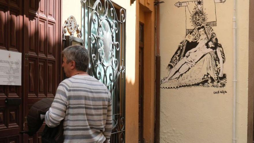 Un hombre lee un cartel en la sede de Nuestra Madre y al fondo, el mural realizado por Saúl Alija.