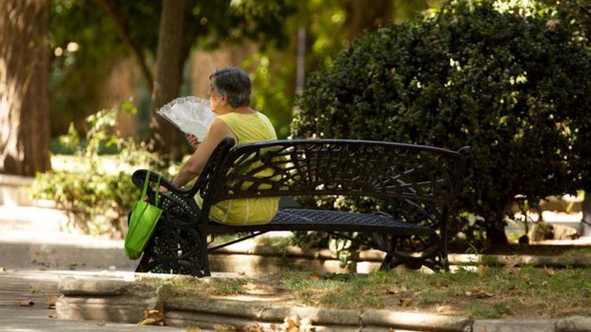 Una mujer se alivia del calor abanicándose en un parque del paseo de Cánovas de Cáceres.