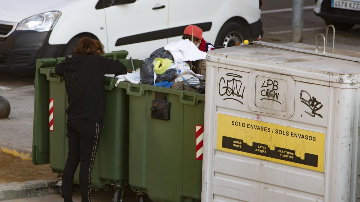 Dos personas rebuscan entre la basura en unos contenedores en Xàtiva.