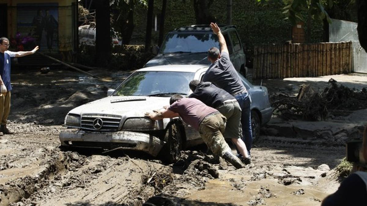 Unos hombres intentan desatascar un coche dañado por las inundaciones, en Valencia.