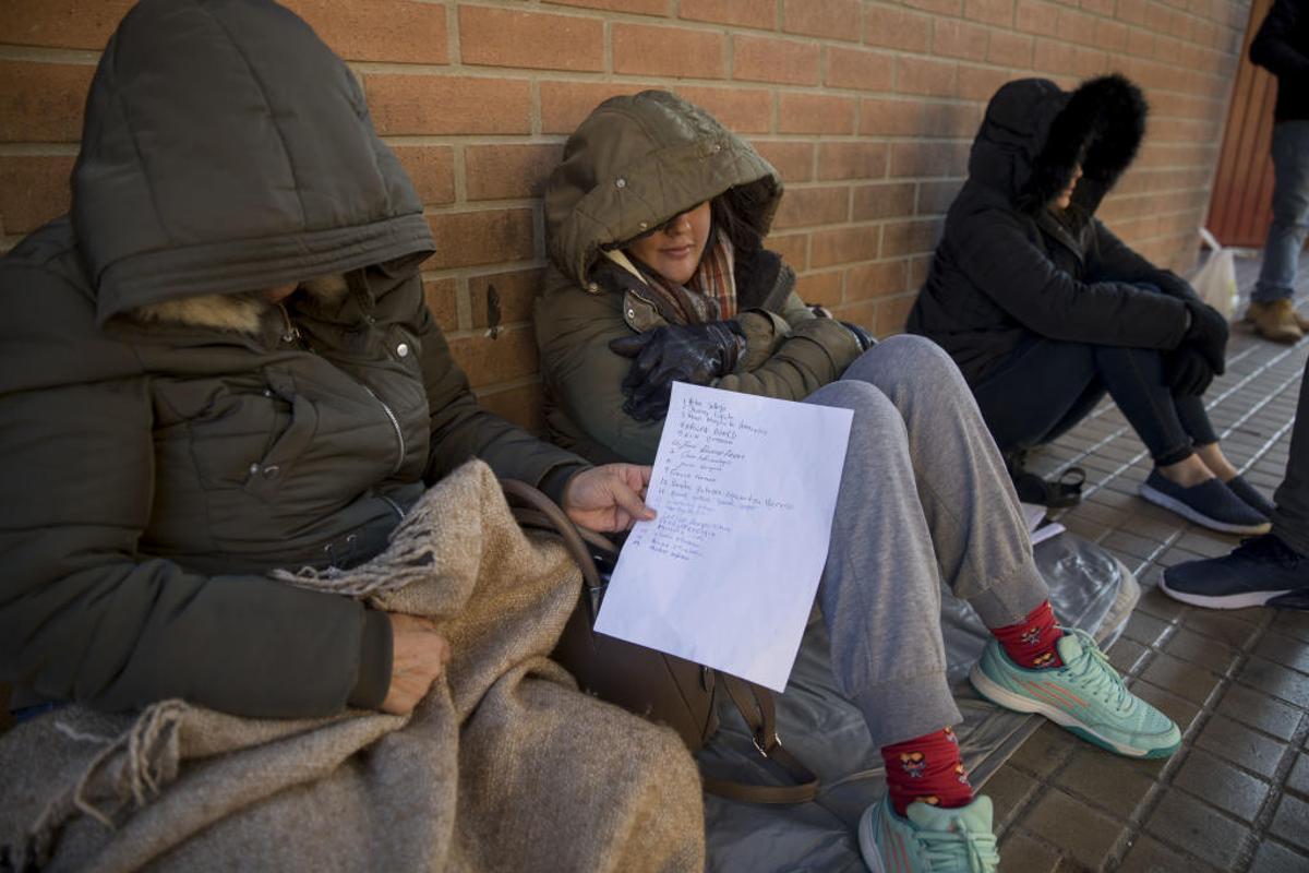 Mujeres migrantes a al espera de la cita previa muestran la hoja donde se apunta el turno.