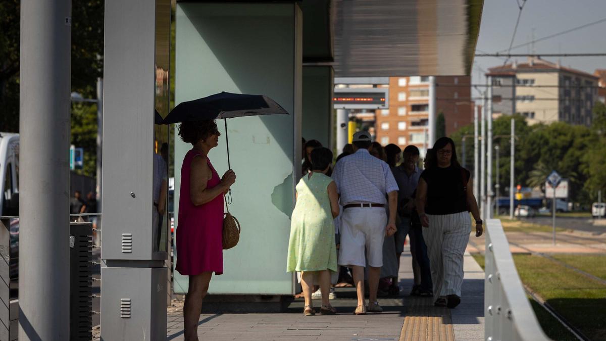 Una mujer se protege del sol en una parada del tranvía, en Zaragoza.