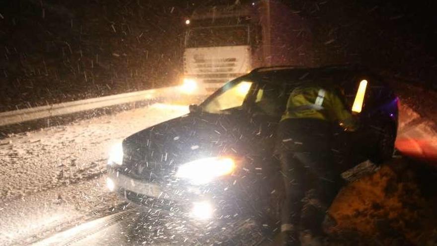 Un guardia de Tráfico ayuda a un turismo en su intento de avance en la nieve, en la A-52. // Nick