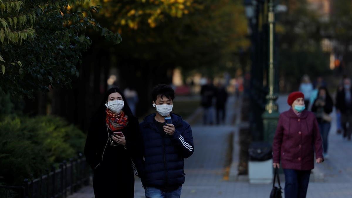 Varias personas con mascarilla pasena por un parque de Moscú, este martes.