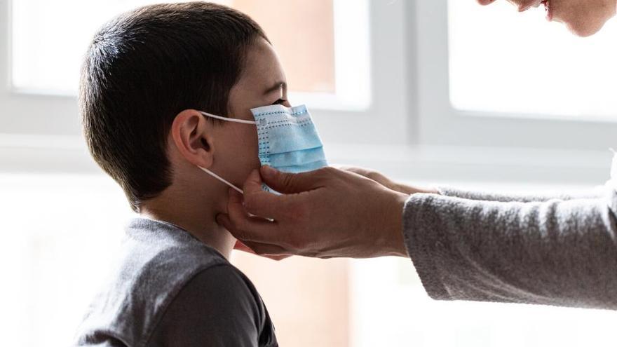 Una madre le coloca a su hijo la mascarilla quirúrgica.