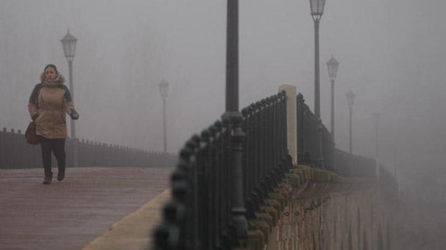 Una mujer cruza el Puente de Piedra de Zamora entre la intensa niebla.