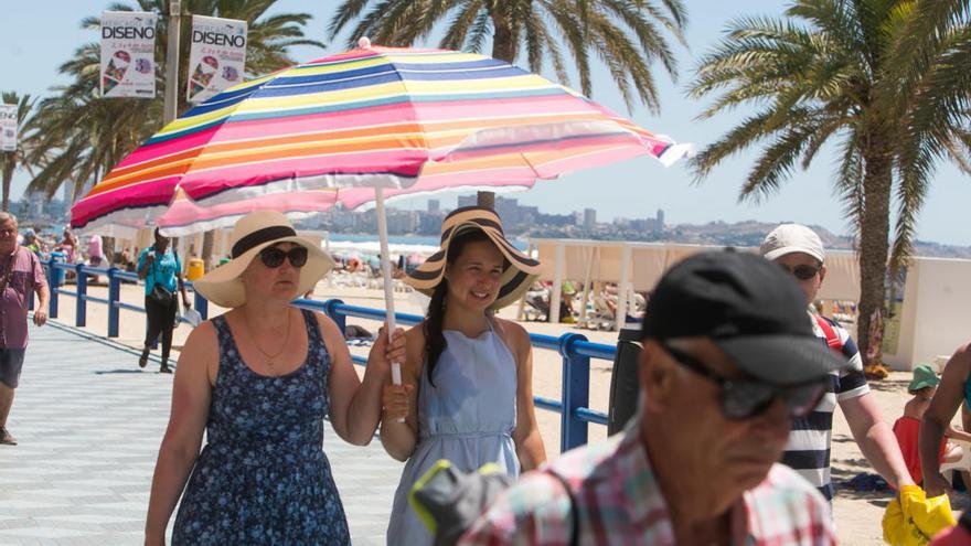 Turistas protegiéndose del sol en el paseo de Gómiz de la Playa del Postiguet en Alicante