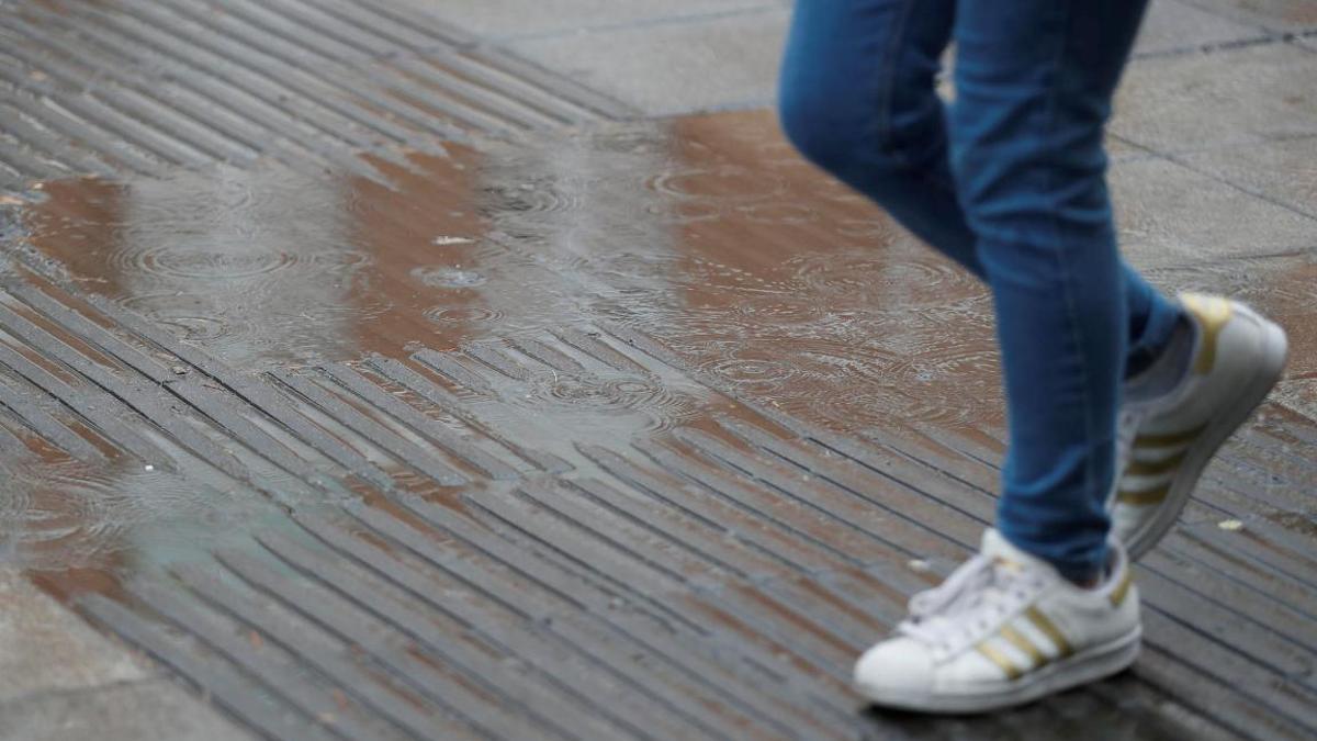 Una persona pasea sobre el suelo mojado por la lluvia