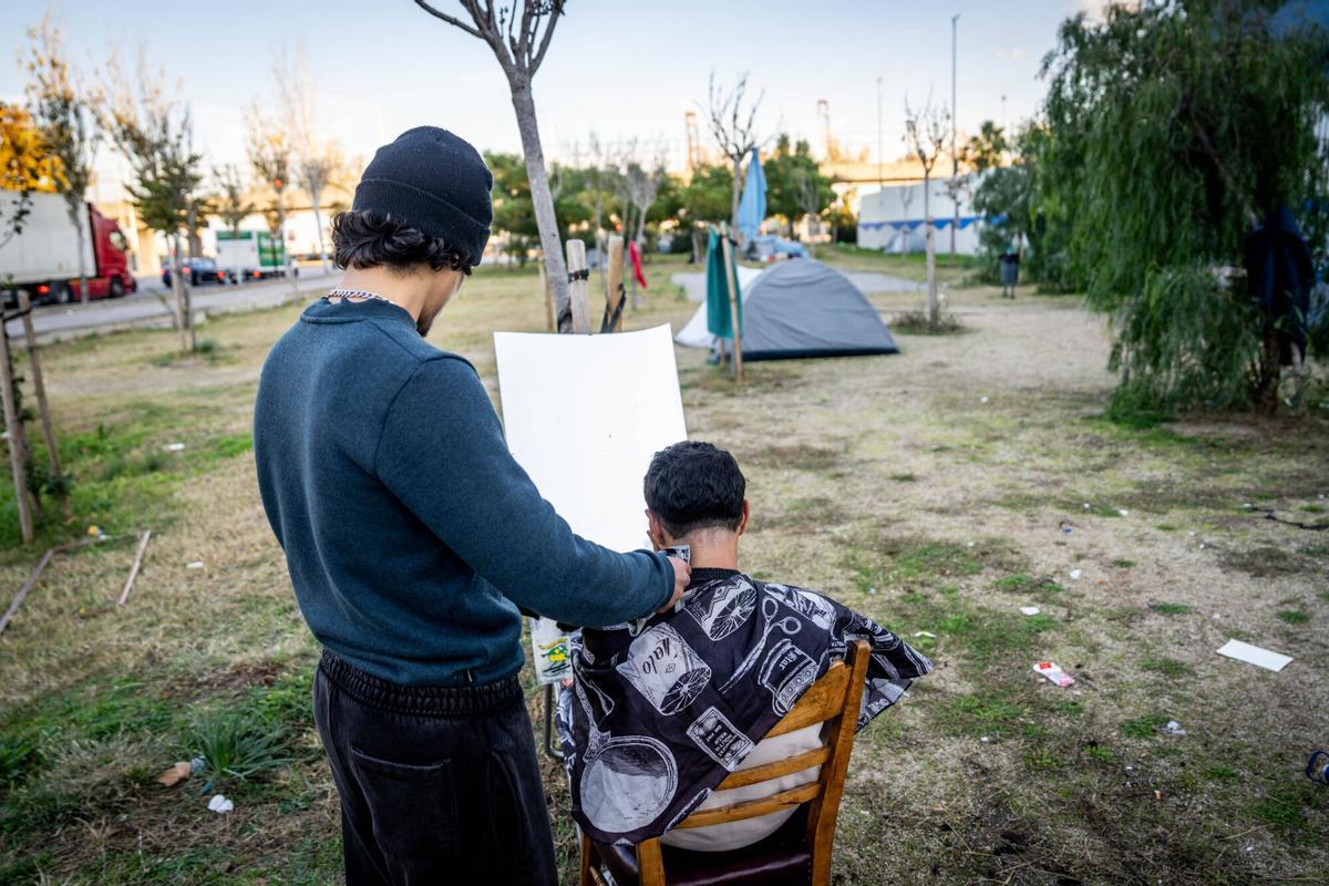 Barcelona 3/12/2025 Sociedad Reportaje sobre las personas sin hogar acampadas en la Zona Franca. - Ya'qub corta el pelo a un amigo que vive con él en la zona de tiendas de campaña donde vive gente sin hogar en la Zona Franca. AUTOR:JORDI OTIX
