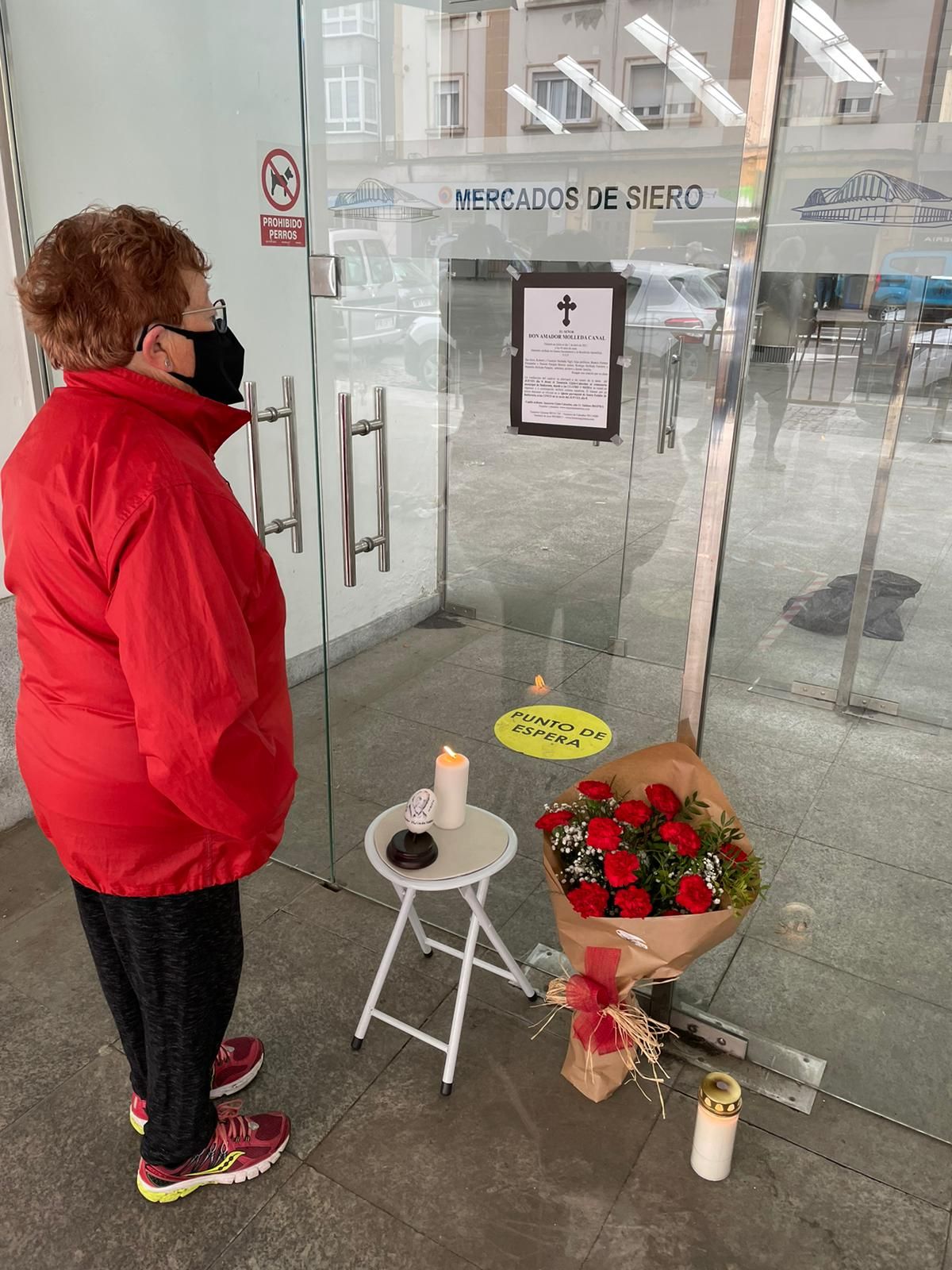 Una mujer lee la esquela de Amador Molleda junto a su puesto de siempre, donde se depositaron flores y velas en su recuerdo.