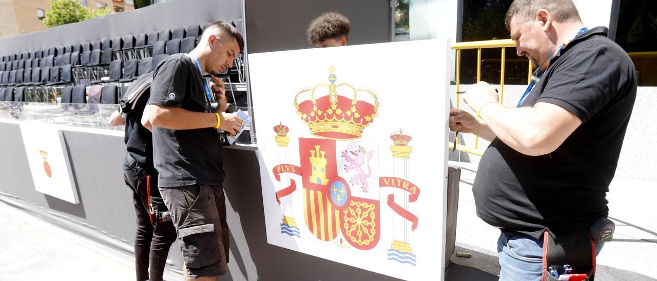 Unos operarios montan el escudo de España en uno de los graderíos para autoridades.
