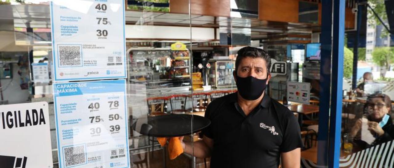 Un camarero de la cafetería Blanca Paz, junto al cartel de aforos que deberán volver a cambiar. |   // ALBA VILLAR