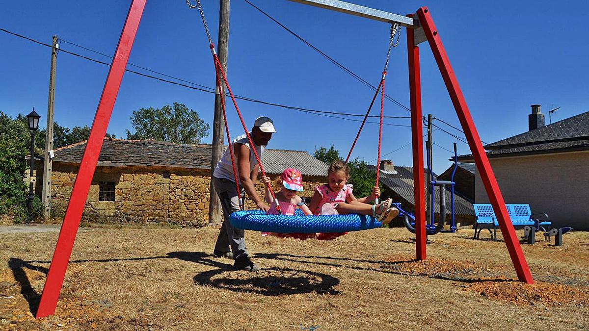 Un hombre ayuda a dos niñas a columpiarse en un pueblo zamorano.