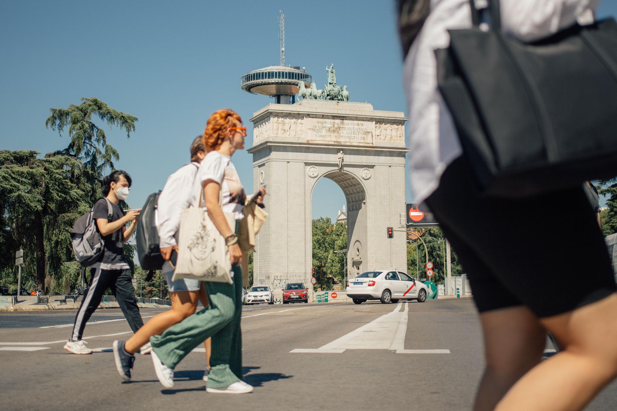 Varios viandantes cruzan un paso de peatones frente al Arco de la Victoria de Moncloa, en Madrid.