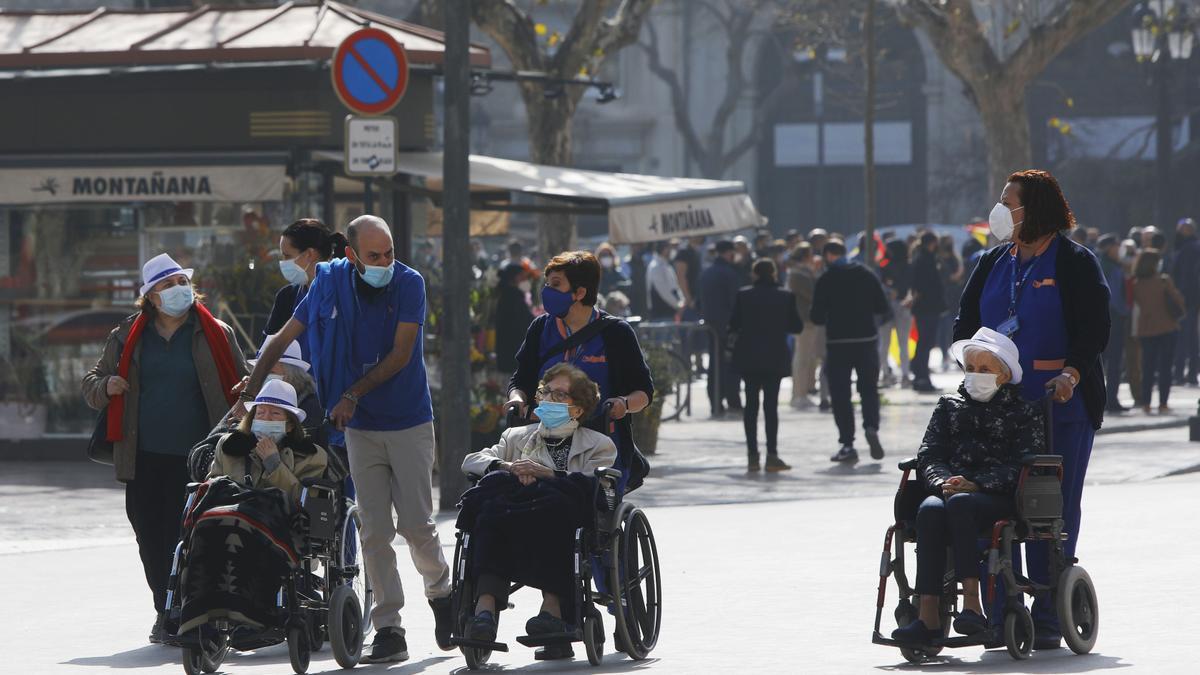 Ancianos en silla de ruedas llevados por sus cuidadores por la plaza del Ayuntamiento.