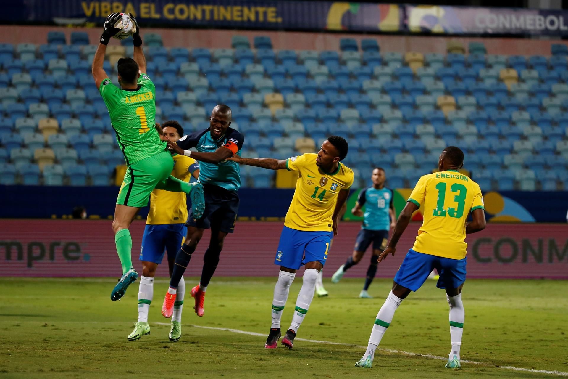 El guardameta brasileño Alisson atrapa la pelota ante la presión de un futbolista ecuatoriano.