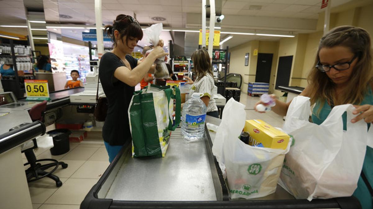 Una clienta con una bolsa ecológica y otra, con bolsas de plástico, en un supermercado.