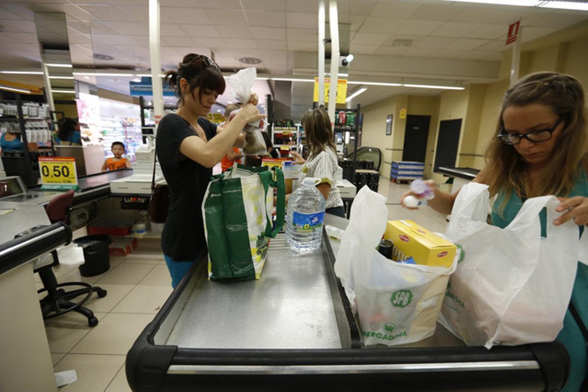 Una clienta con una bolsa ecológica y otra, con bolsas de plástico, en un supermercado.
