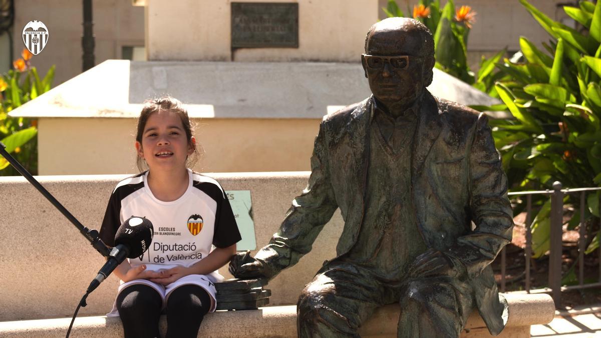 Una de les xiquetes d'Escoles Cor Blanc i negre recintat el poema 'Assumiràs la veu d'un poble' de Vicent Andrés Estellés al costat de l'estàtua del poeta a Burjassot.