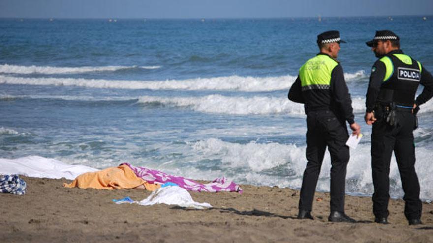 Dos agentes de la Policía Local de Marbella custodian los tres cadáveres en la playa de La Venus.