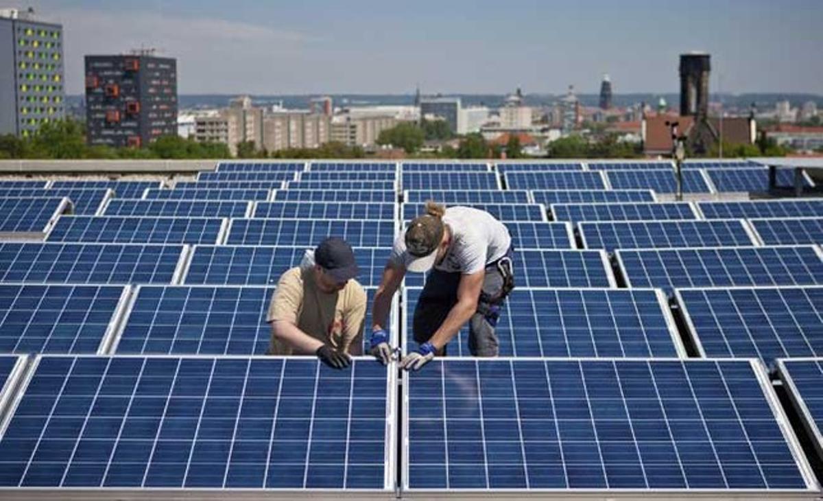 Dos operaris col·loquen panells solars a la teulada de l’edifici Gerber de la Universitat Tecnològica a Dresden (Alemanya) aquest dimarts. El sistema s’està construint amb motiu de la celebració del Congrés de l’Església Protestant.