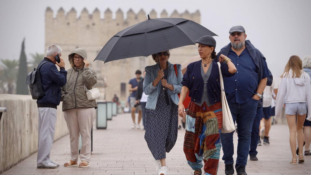 Varias personas caminan bajo la lluvia este lunes, en el Puente Romano de Córdoba.
