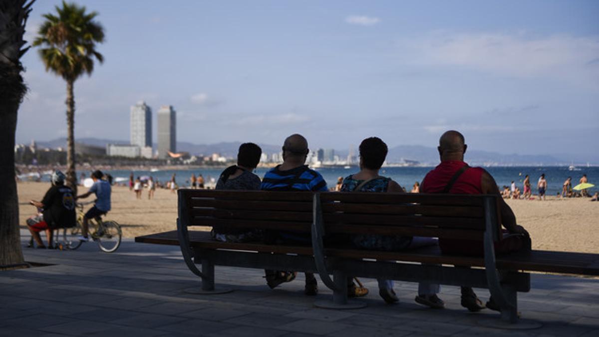 Dos parejas observan la animada vida del paseo junto al mar en la playa de la Barceloneta.