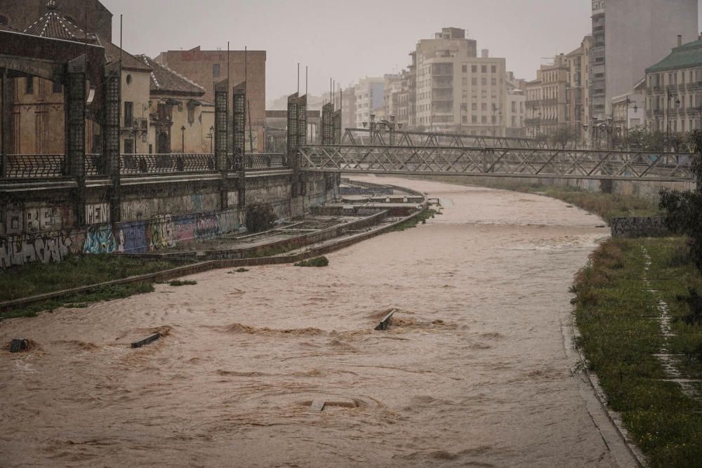 El río Guadalmedina crecido con agua y calles del Centro y el entorno del cauce, desiertas bajo la lluvia, la estampa de este martes 31 de marzo.