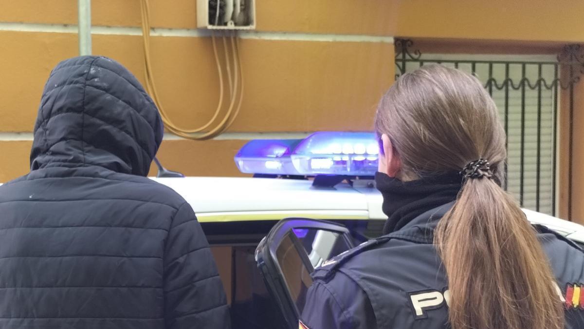 Una agente de la Policía Nacional traslada al coche policial a uno de los detenidos.