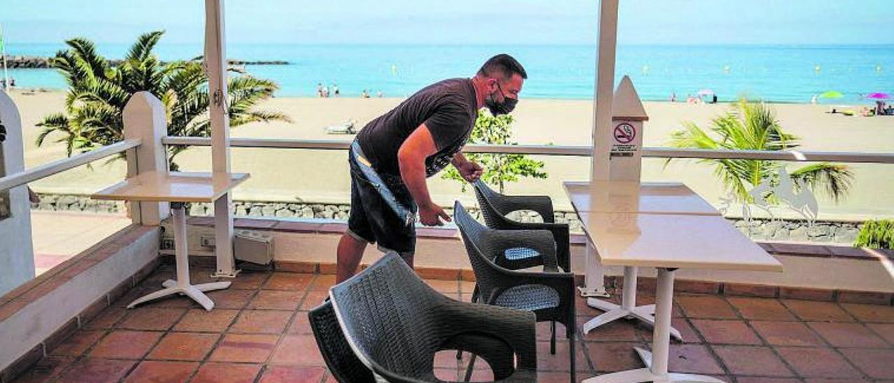 Un trabajador recoge las mesas de una terraza en el paseo de la playa de Los Cristianos, en el sur de Tenerife.