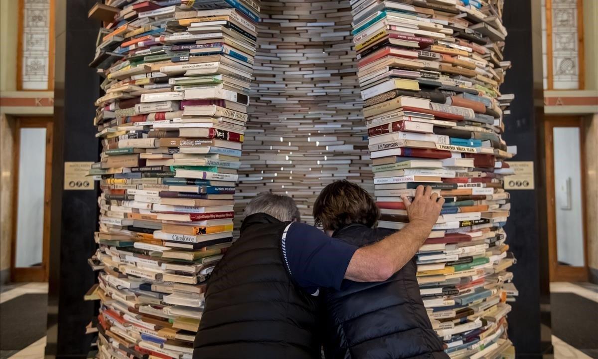 Dos personas observan la escultura titulada Idioma del artista eslovaco Matej Kren, una columna hecha de 8.000 libros, expuesta en la entrada de la Biblioteca Central de Praga (República Checa) durante la celebración del Día del Libro. 