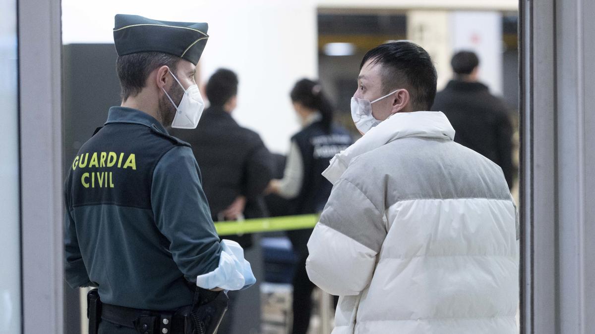 Un agente de Guradia Civil con un pasajero que llega al aeropuerto Adolfo Suárez Madrid-Barajas procedente de un vuelo de Chongqing (China), a 3 de enero de 2023, en Madrid (España).