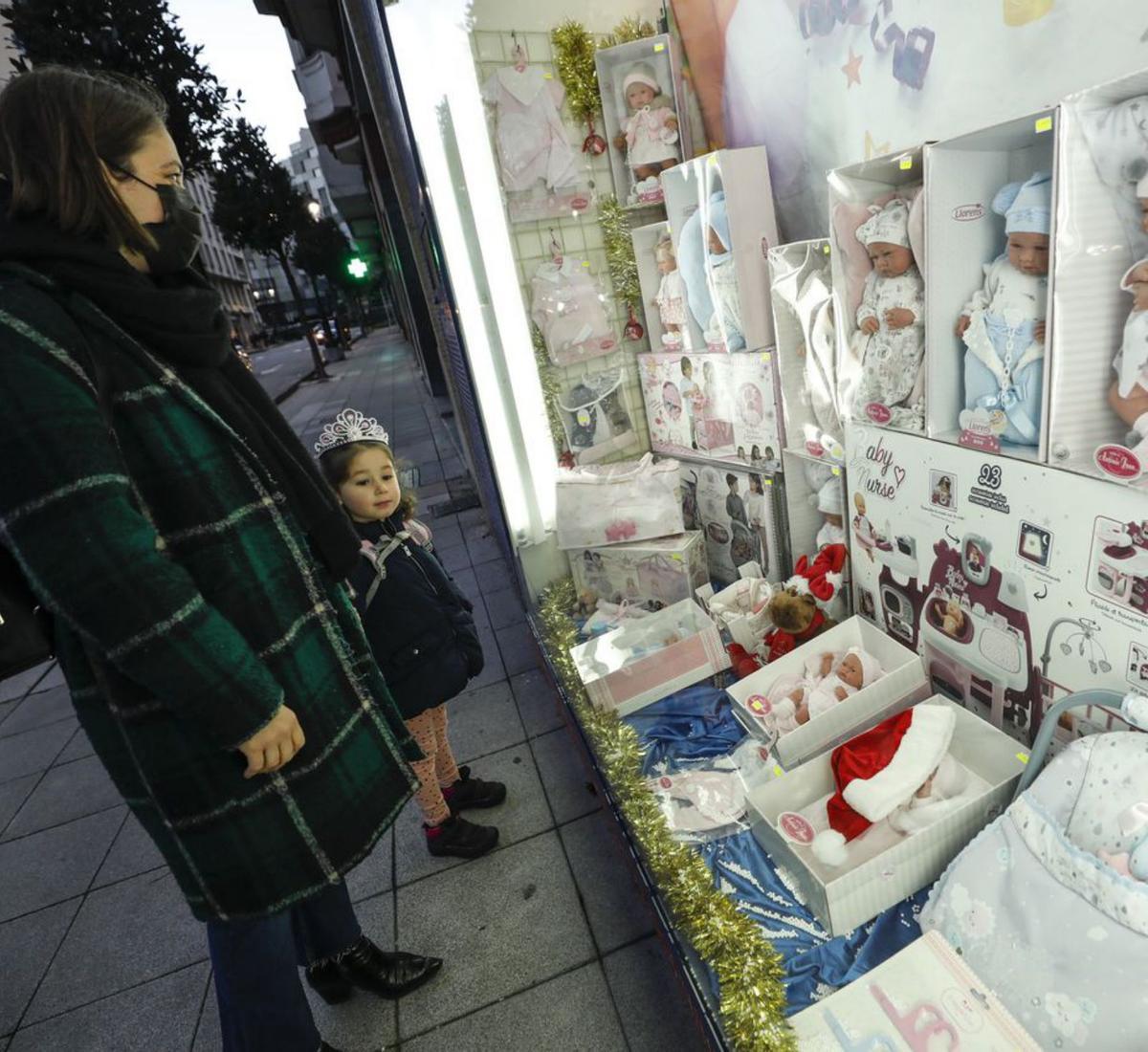Arriba, Lorena Riesco y Martina Lago en el escaparate de una juguetería ovetense. En el círculo, dos niñas observan los juguetes de otra tienda, cuya responsable, Paula Palazón, coloca un gran peluche en la última foto. | Luisma Murias