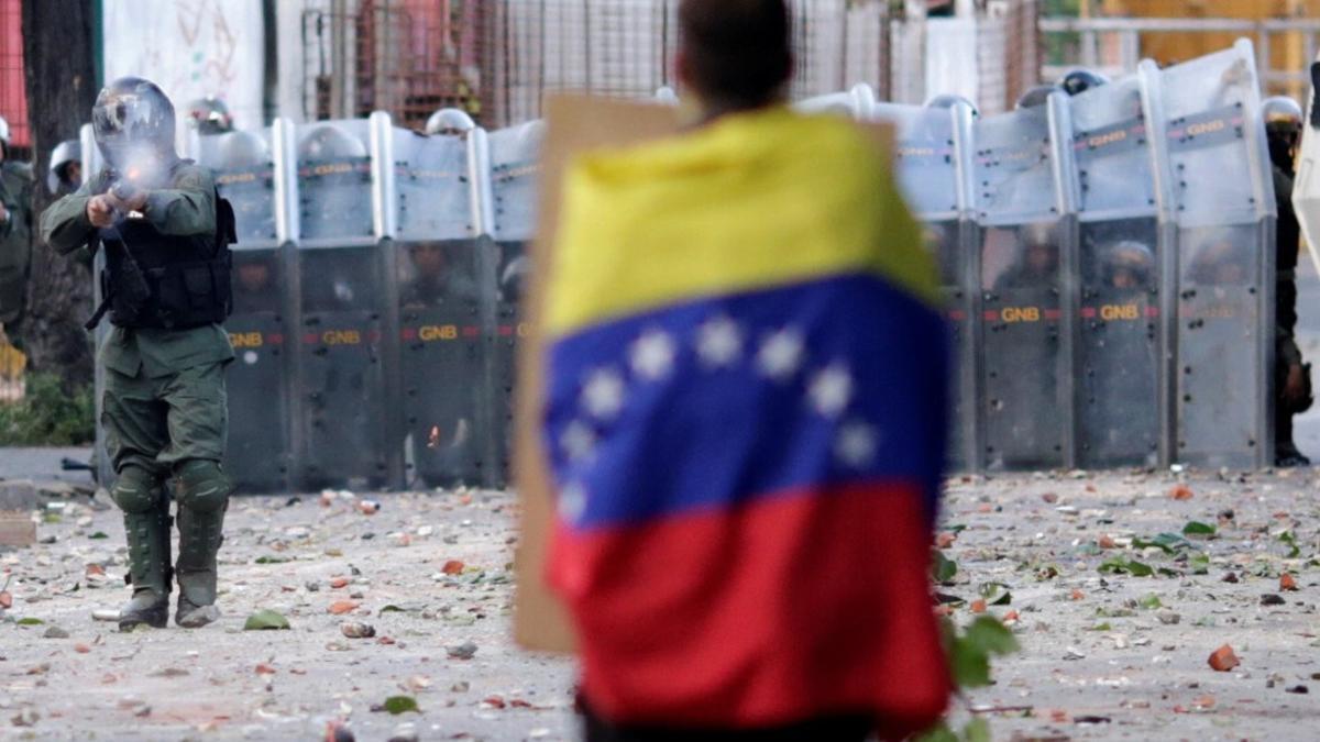 A man with a Venezuelan flag stands in front of riot security forces while rallying against Venezuela's President Nicolas Maduro's government in Caracas