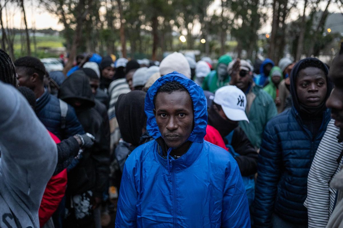 Un grupo de migrantes hace cola en el exterior de Las Raíces para coger comida que les lleva una oenegé.