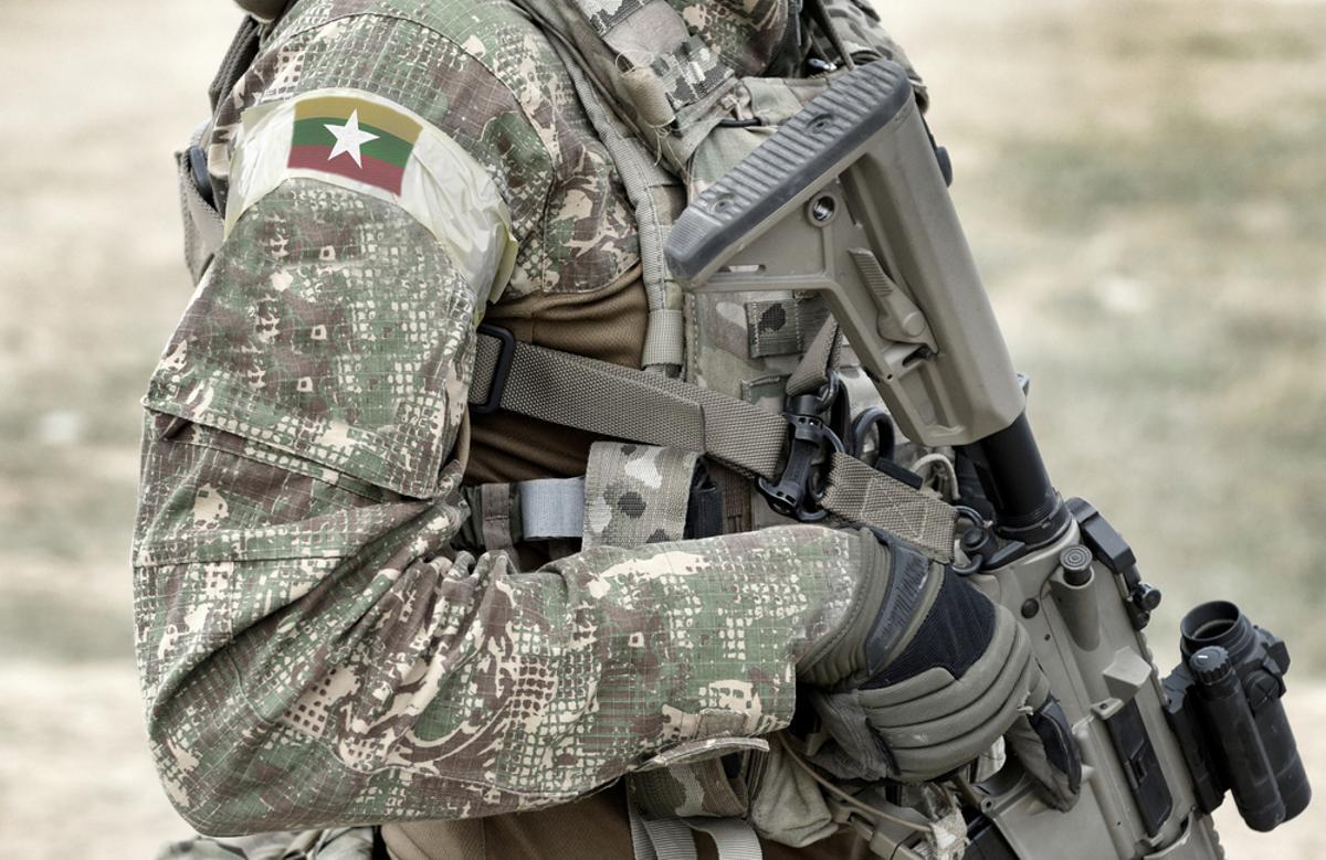 Soldado con rifle de asalto y bandera de Birmania con uniforme militar.