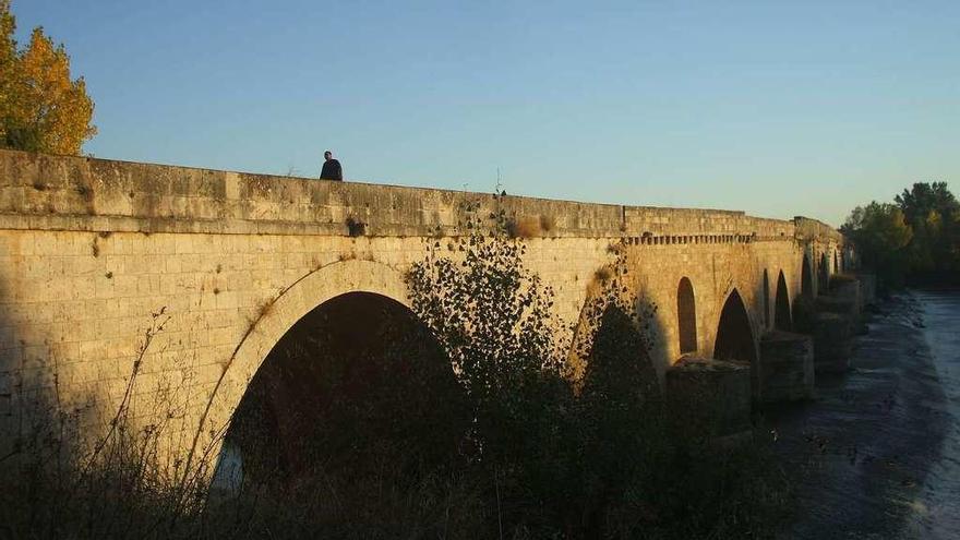 Un vecino pasea por el tablero del puente de piedra que está previsto restaurar.