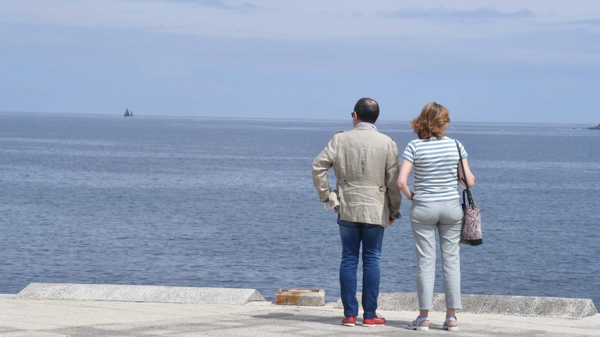 Dos personas observan el mar desde el paseo marítimo coruñés.