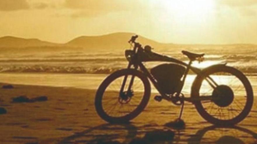 Una bicicleta eléctrica sobre la arena de la orilla de Famara al atardecer.
