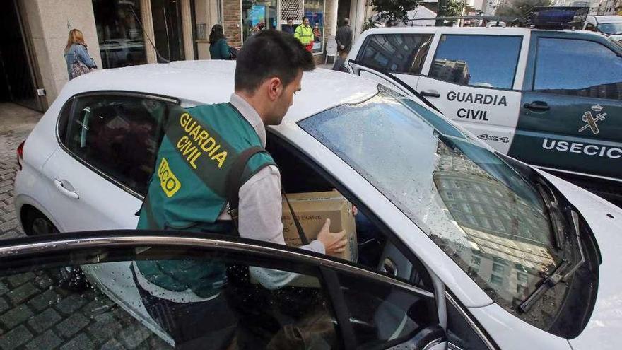 Un agente introduce en el coche una caja con documentación incautada en un registro en Rosalía. // M.G. Brea