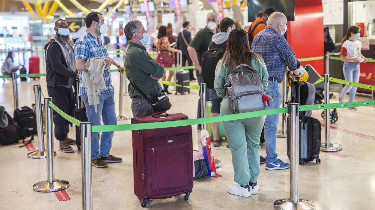 Varias personas hacen fila con maletas en la terminal T4 del aeropuerto de Barajas.