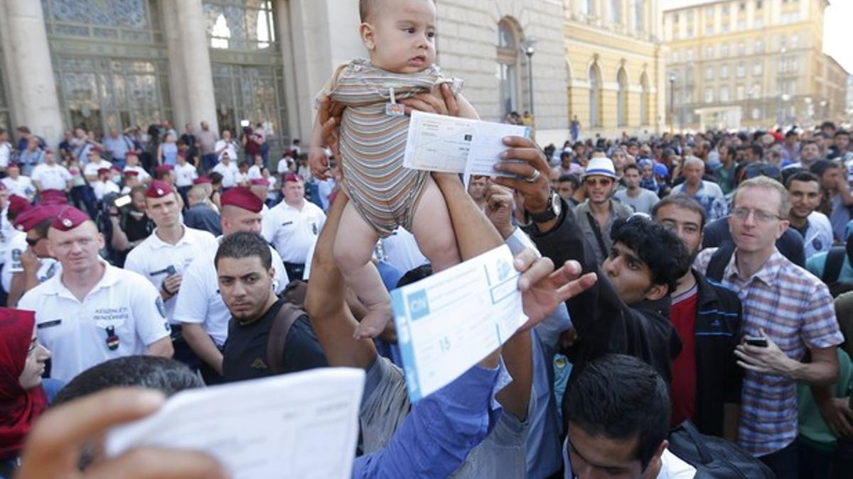 Un inmigrante sirio levanta a su hijo ante la policía húngara para pedir que reabran la estación de trenes de Keleti mientras otros muestran sus billetes.