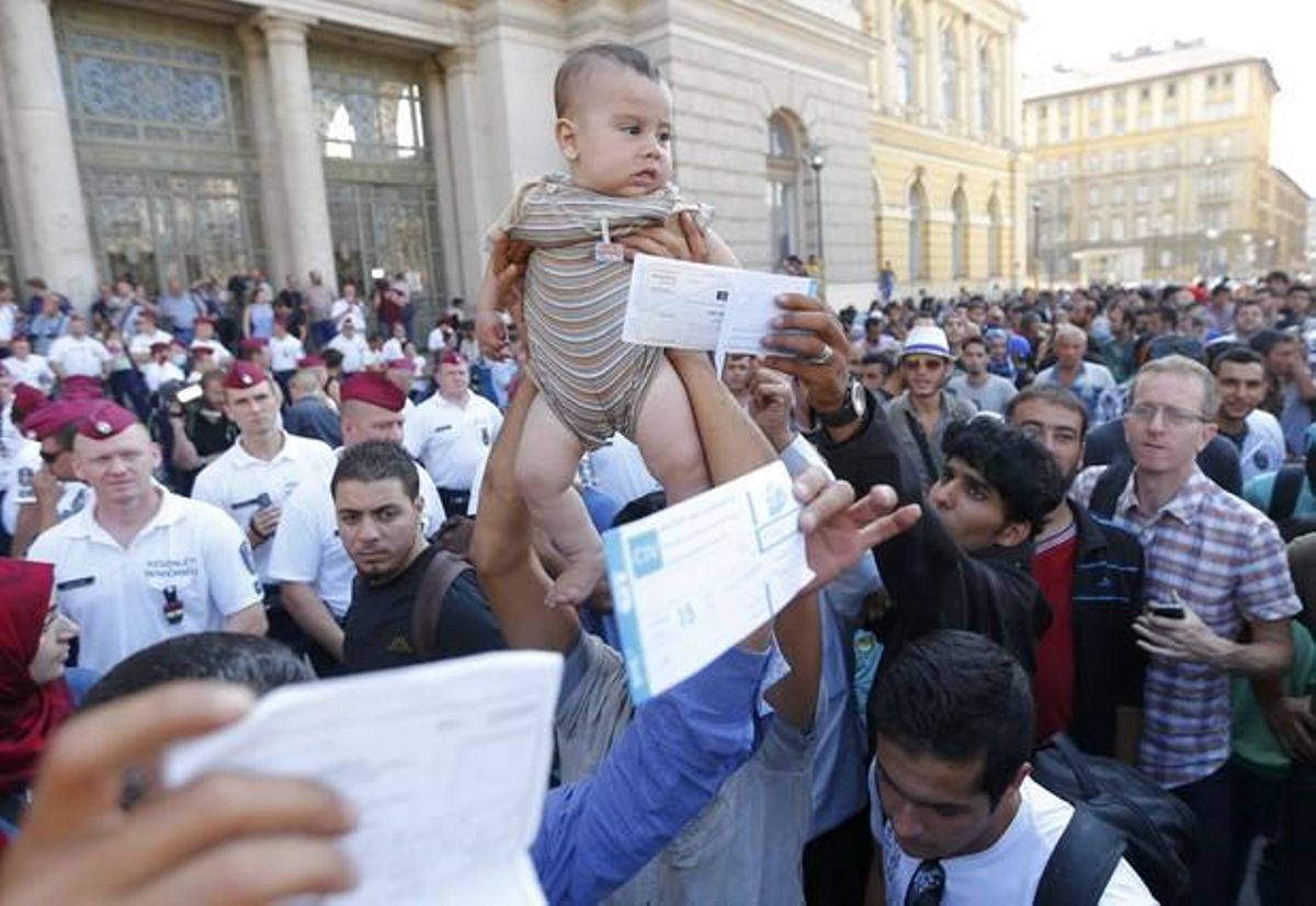 Un inmigrante sirio levanta a su hijo ante la policía húngara para pedir que reabran la estación de trenes de Keleti mientras otros muestran sus billetes.