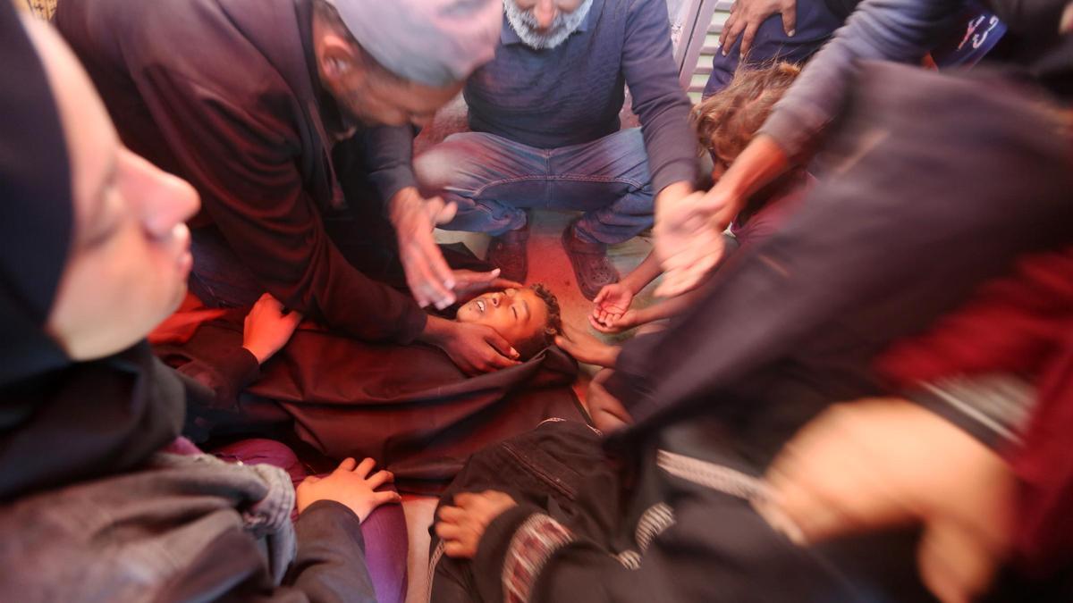 Un grupo de palestinos velan el cuerpo de un familiar muerto en un bombardeo israelí en un campo de desplazados de Deir al Balah, este martes.