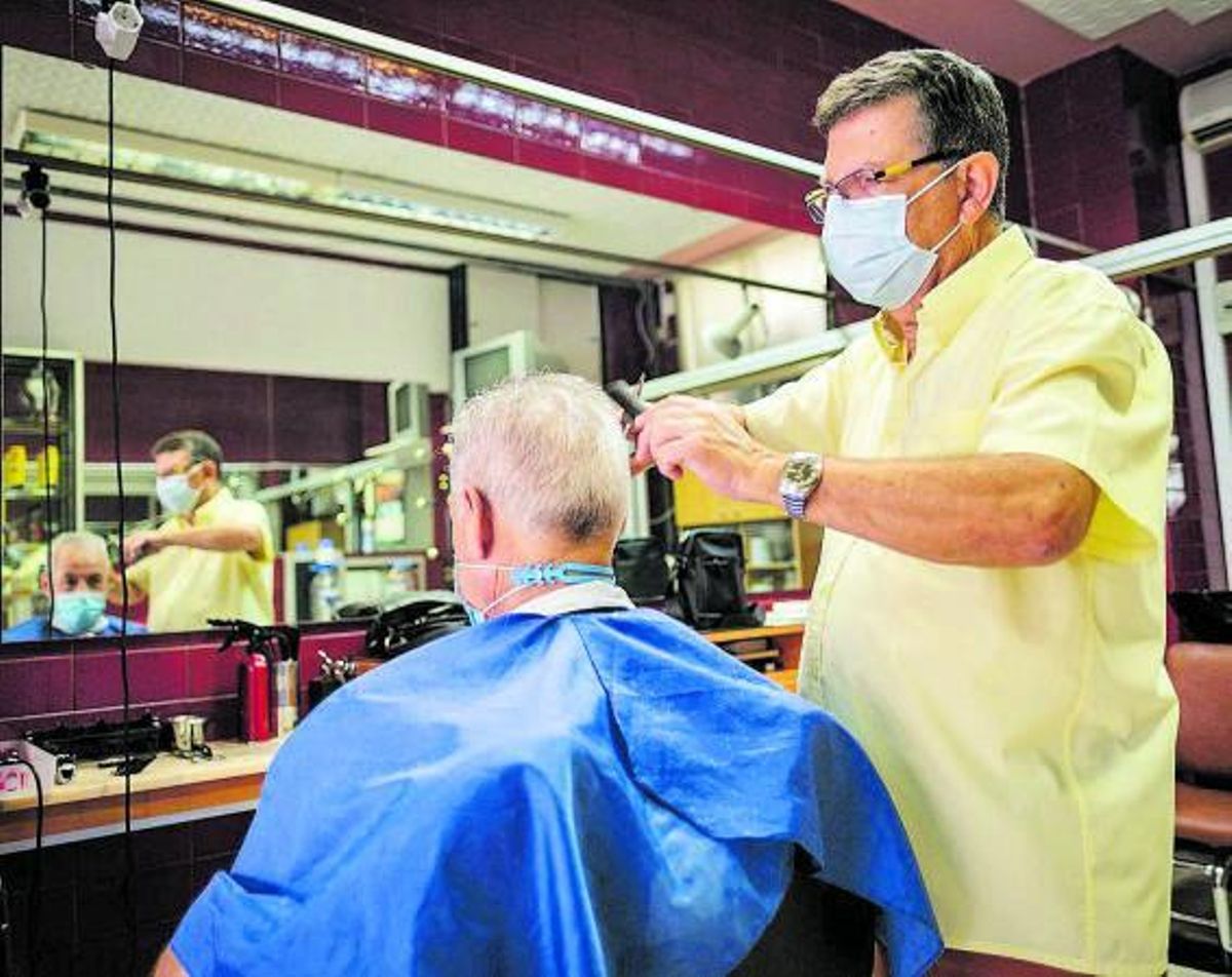 Un peluquero con un cliente en su peluquería. | ANDRÉS GUTIÉRREZ