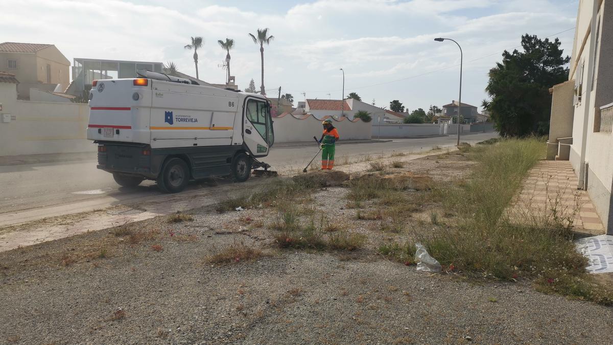 Un operario del servicio de limpieza municipal de Torrevieja corta las matas en la acera de la avenida Andradas sin actuar en la parcela anexa, de la que nadie se hace responsable