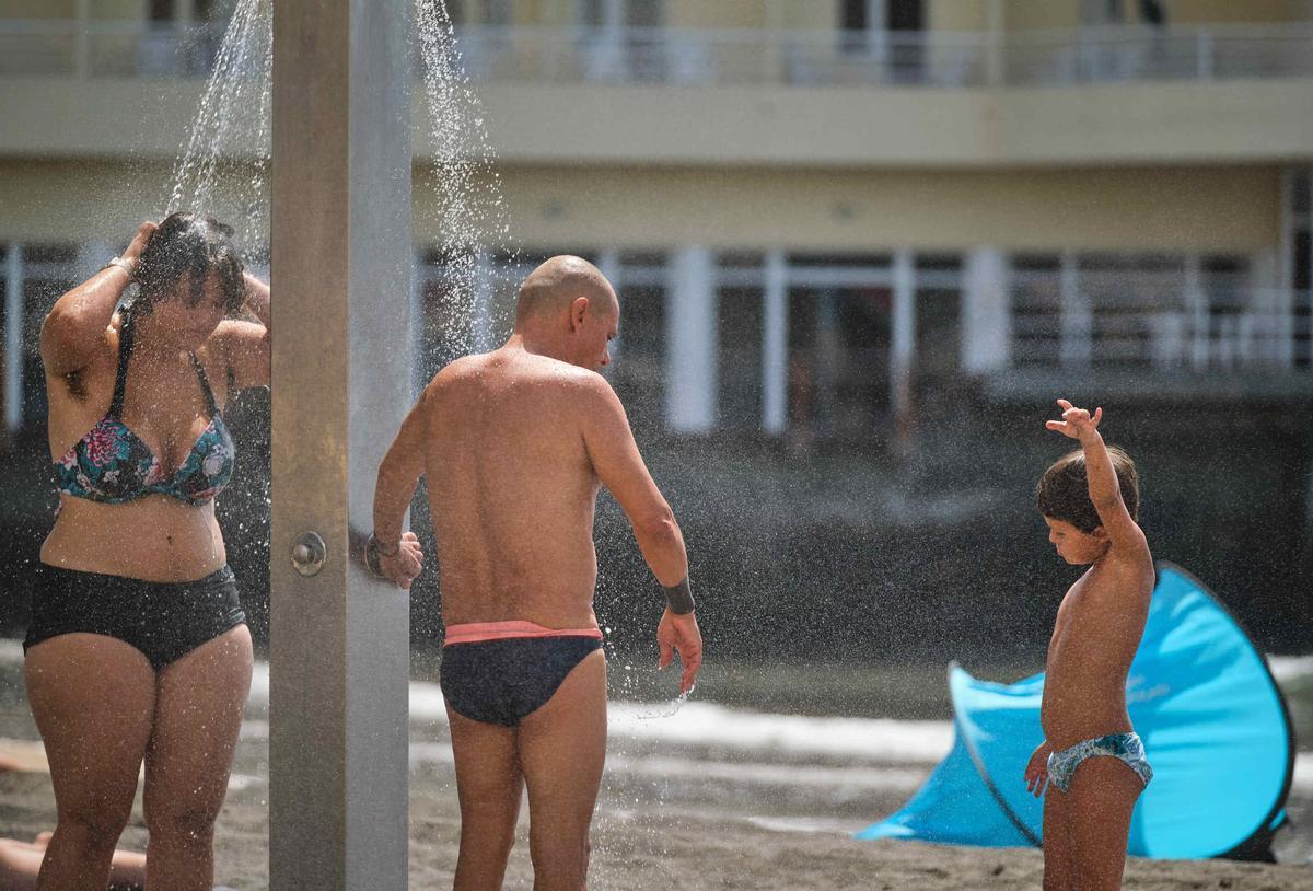 Varias personas se duchan en una playa de El Medano para mitigar el calor.